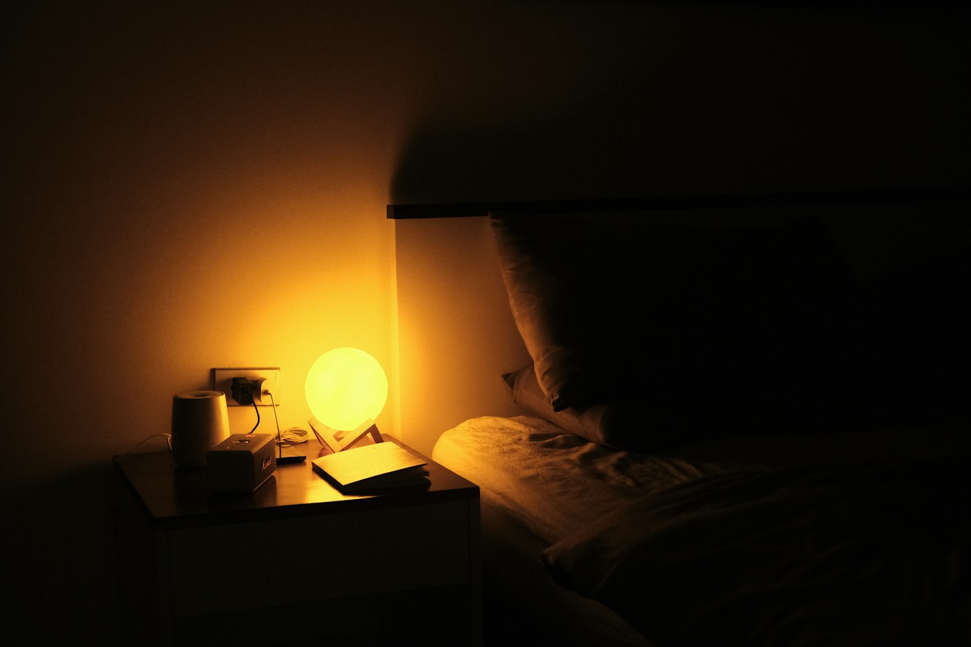 A bedside table and warm lamp in a quiet bedroom at night