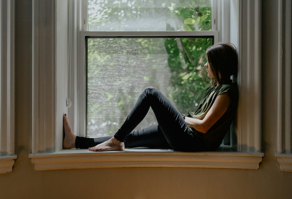 Woman sitting quietly by a window, reflecting on feeling emotionally disconnected