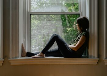 Woman sitting quietly by a window, reflecting on feeling emotionally disconnected