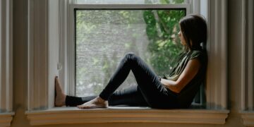 Woman sitting quietly by a window, reflecting on feeling emotionally disconnected