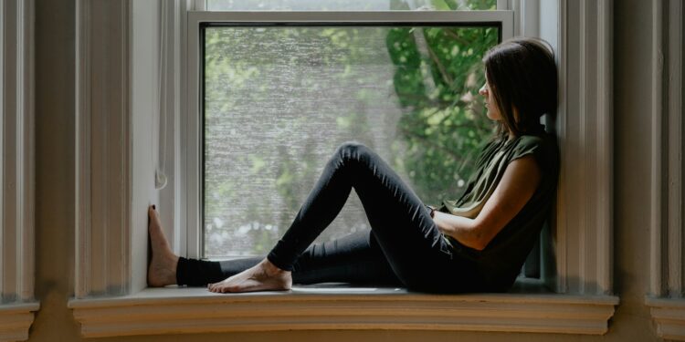 Woman sitting quietly by a window, reflecting on feeling emotionally disconnected