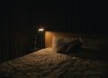 A softly lit bedside lamp beside a bed at night, creating a calm setting for winding down before sleep