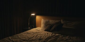 A softly lit bedside lamp beside a bed at night, creating a calm setting for winding down before sleep